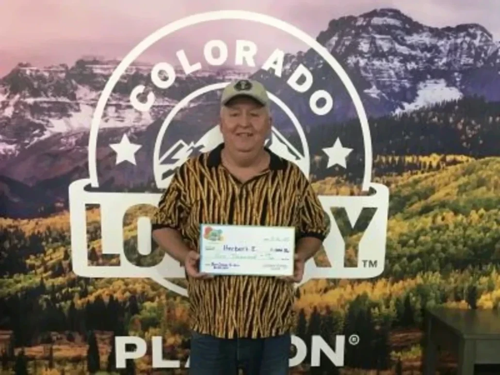 赫伯特·E·在科罗拉多彩票背景前手持一张超大支票，金额为$1,000